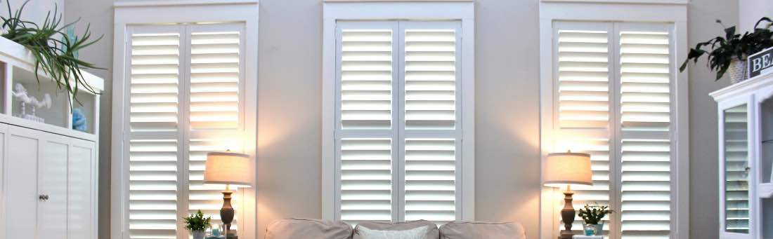 White Polywood shutters on three living room windows behind a sofa